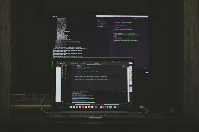 Laptop and monitor displaying code for web application testing.
